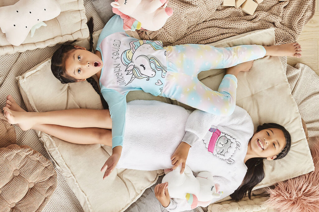 two kids laying in a bed of pillows wearing Cozy pyjamas