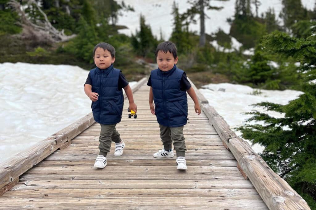 young twins running along wooden walkway in the snow and mountains
