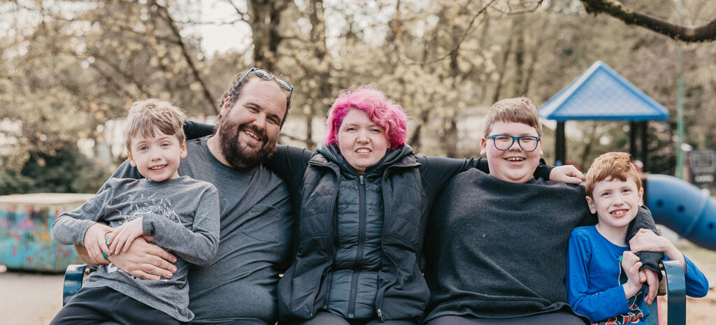 Family with three sons sitting on a park bench.