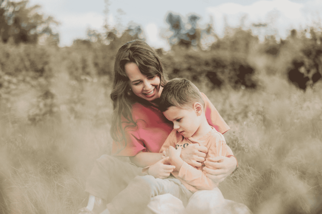 Davyd, who has cerebral palsy, cuddles in his mom Olena's lap in a field of long grass.