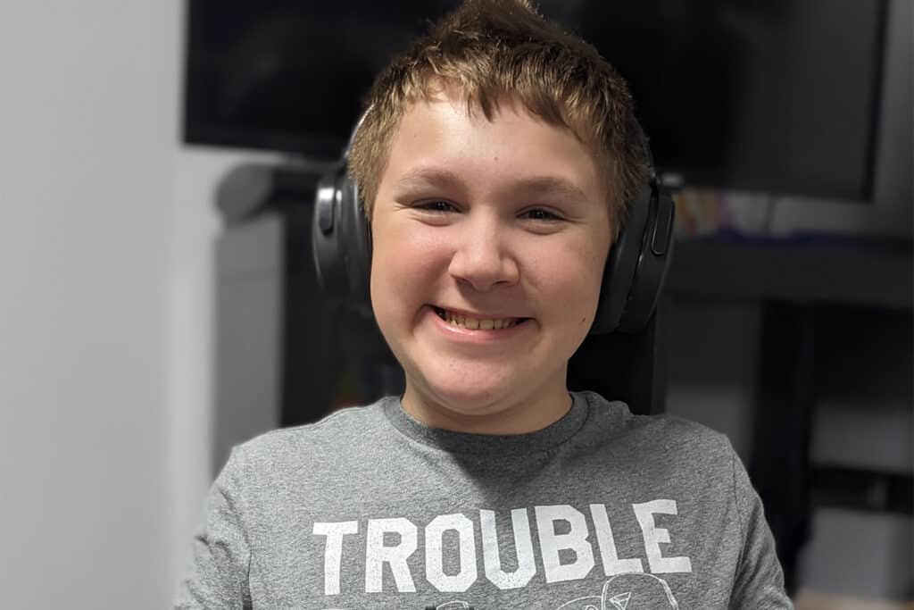 Coltrane smiles at camera wearing a gray t-shirt and noise-cancelling headphones.