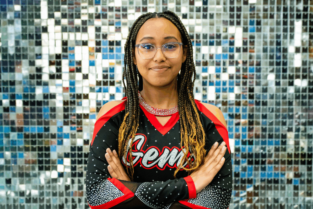 A young woman with braids wearing a cheer uniform and smiles at the camera